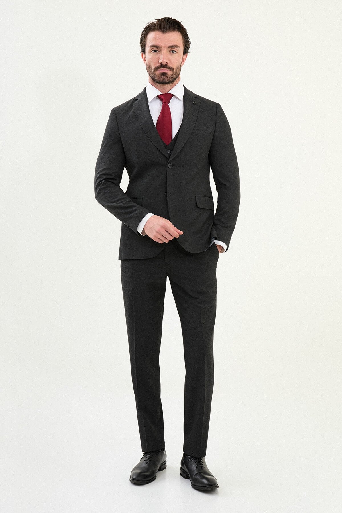 Men’s matte black slim-fit three-piece wool-blend suit with single-breasted jacket, V-neck waistcoat, slim tapered trousers, tonal buttons, and origami lapel pin.