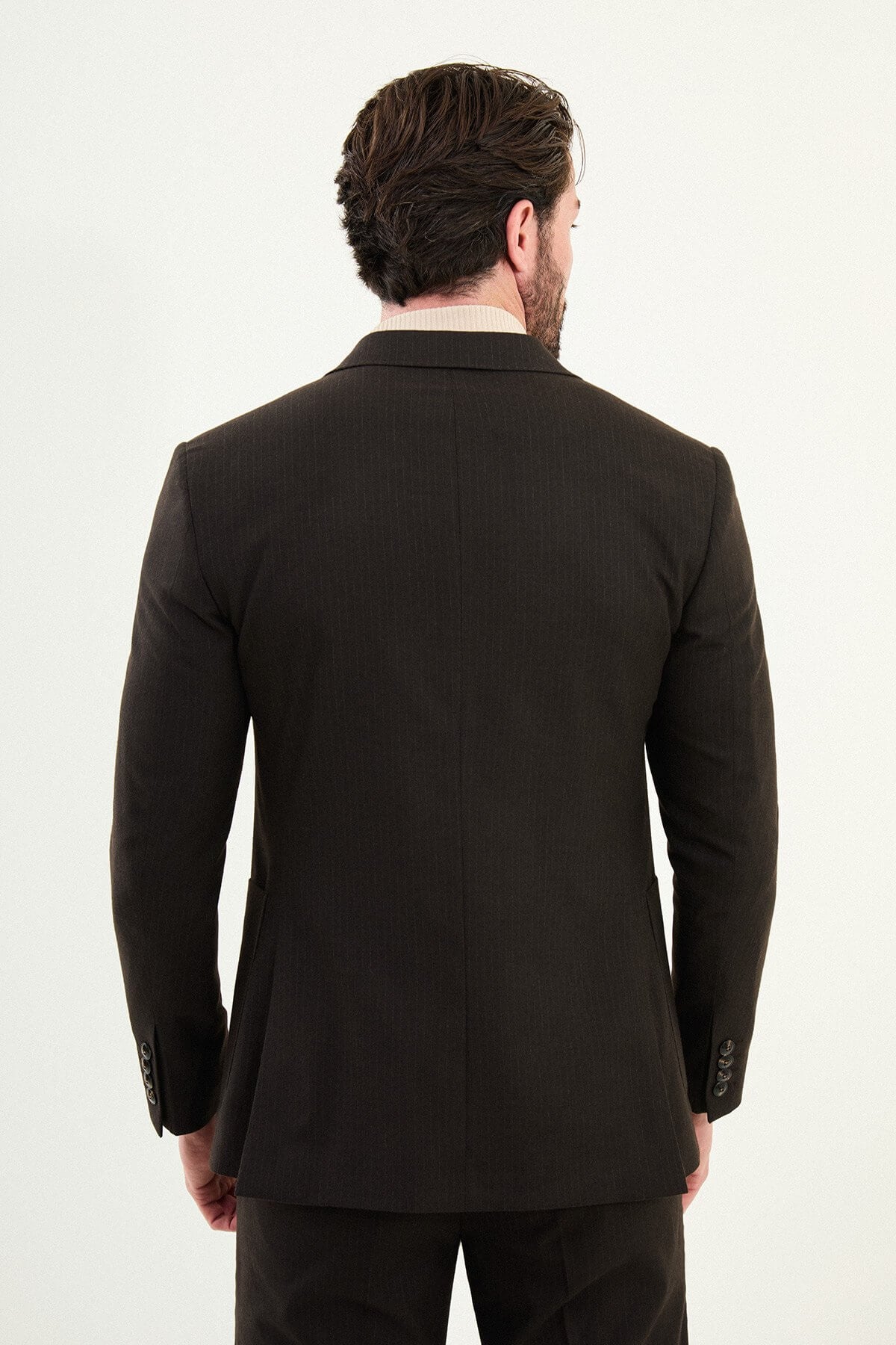 Men’s deep brown slim-fit mono-collar (mandarin collar) performance suit with single-breasted jacket, patch pockets, matte micro-texture fabric, styled with a cream turtleneck.