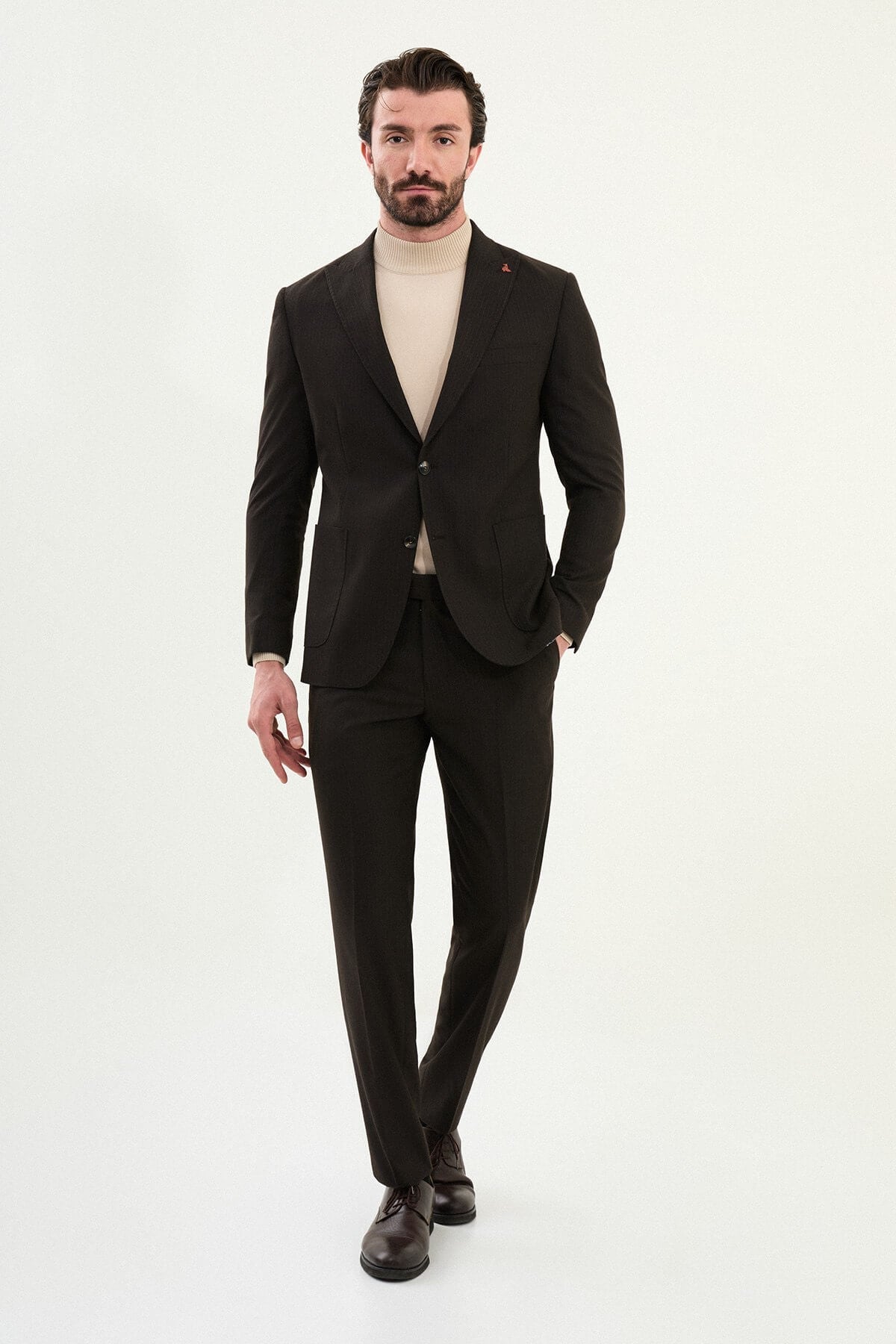 Men’s deep brown slim-fit mono-collar (mandarin collar) performance suit with single-breasted jacket, patch pockets, matte micro-texture fabric, styled with a cream turtleneck.