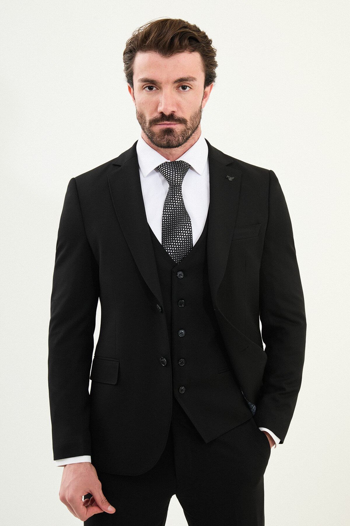 Men’s matte black slim-fit three-piece wool-blend winter suit with single-breasted jacket, notch lapels with AMF stitching, high-cut five-button waistcoat, tapered trousers, and black origami lapel pin.