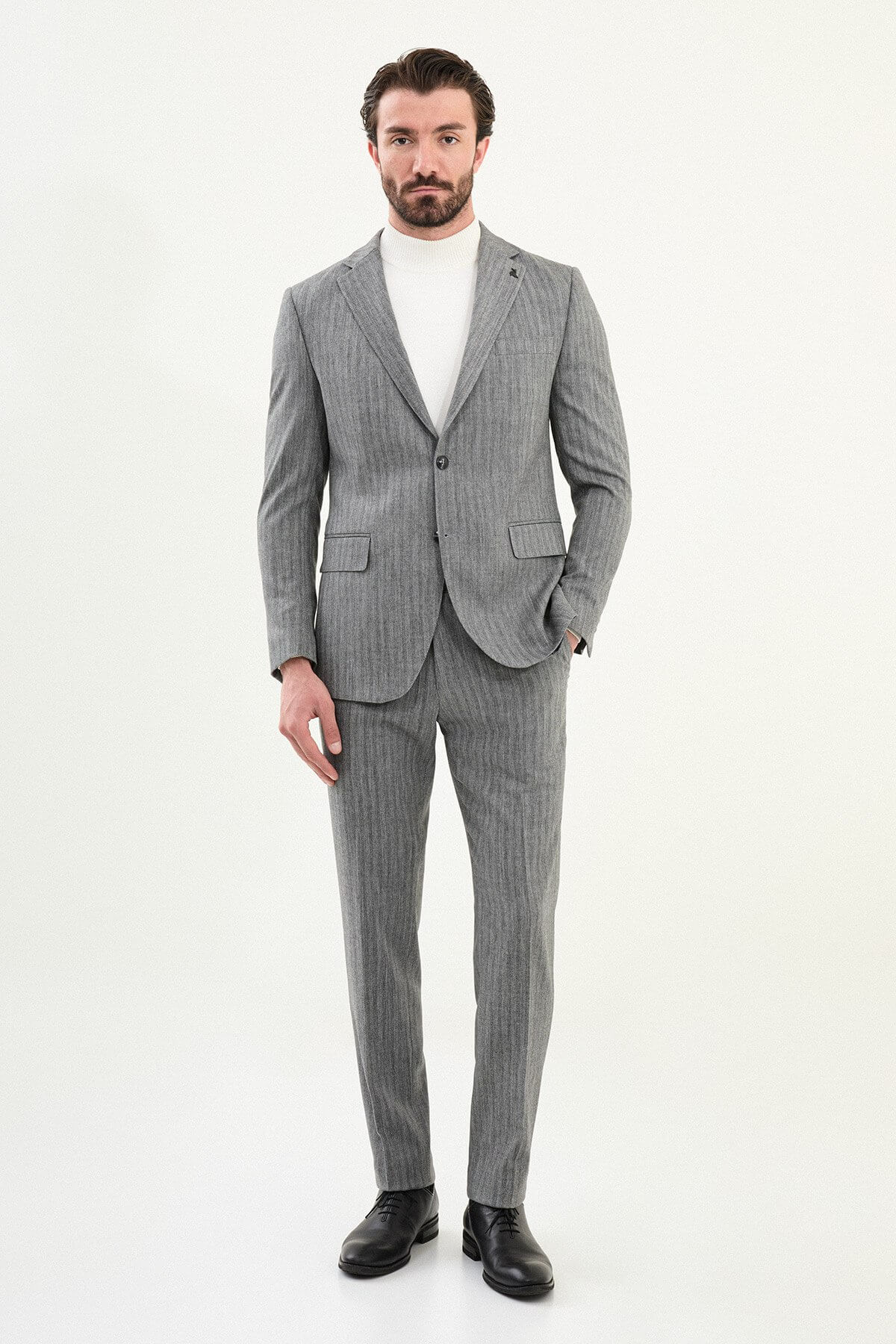 Men’s gray herringbone slim-fit single-breasted suit with structured shoulders and tailored waist, high-wool blend fabric with stretch, styled with a light gray fine-gauge turtleneck for winter.